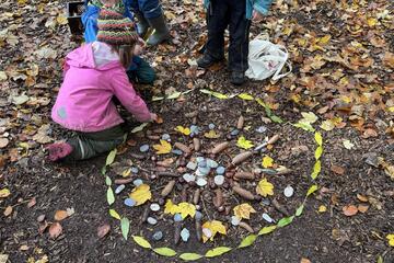 Kinder bauen einen Kreis aus Steinen, Tannenzapfen und Blättern