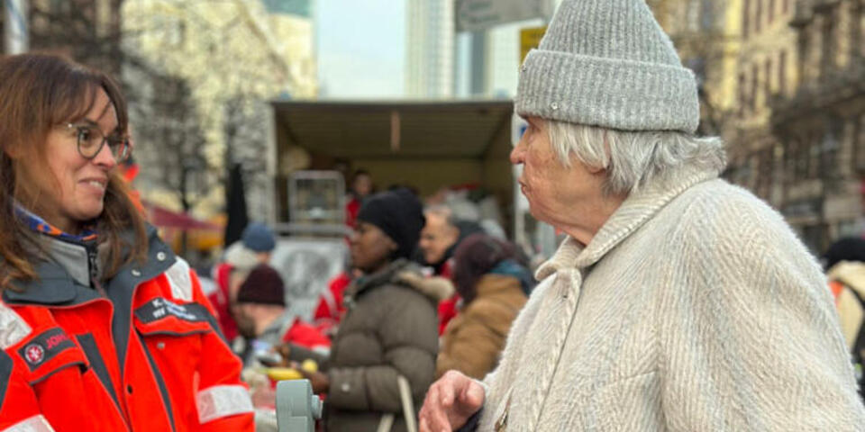 Eine Frau in Johanniter-Uniform unterhält sich mit einer älteren Frau bei der Johanniter-Suppenküche. 