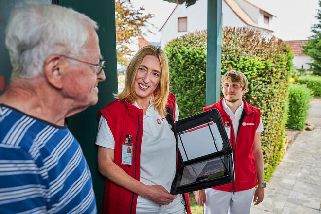 Johanniter Förderservice im freundlichen Gespräch mit älterem Herren an der Haustür.