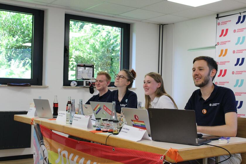 Die vier Mitglieder der Landesjugendleitung sitzen an einem Tisch mit Blick auf die Versammlung.