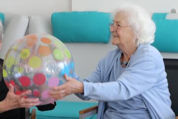 Seniorin hält einen großen Ball in Händen.