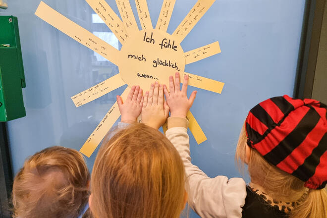Kinder fassen eine Sonne aus Pappe an. Auf der Sonne steht "Was mich glücklich macht"