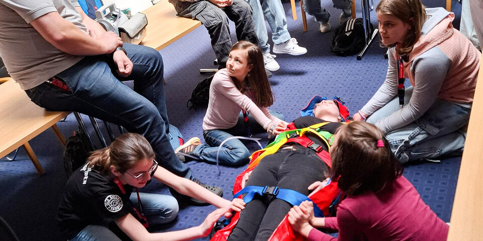 Kinder wickeln eine Person in einer Rettungdecke