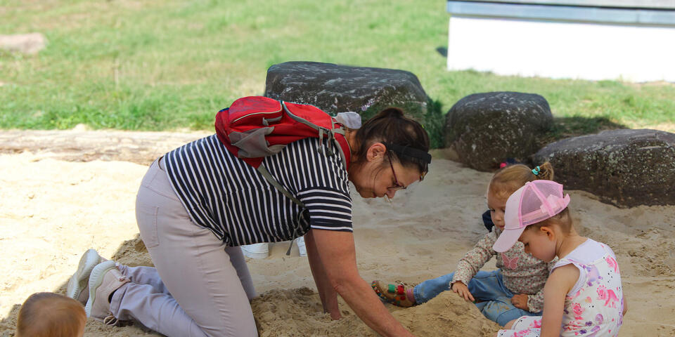 Eine Frau spielt mit zwei Kindern im Sand