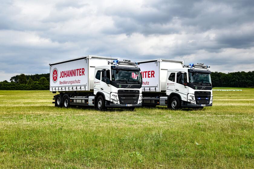Zwei große weiße Logistik-LKW stehen versetzt nebeneinander. Auf der Plane des Containers ist das Logo der Johanniter zu sehen.