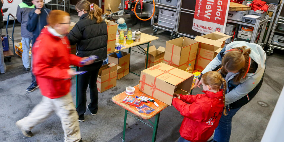 In einer Halle packen Jugendliche gemeinsam Spendenkartons für bedürftige Familien.