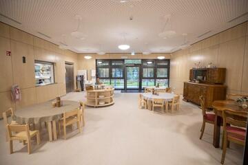 Ein Ausblick auf die Cafeteria mit runden Tischen, alter Kommode und dem Fenster zur Küche.