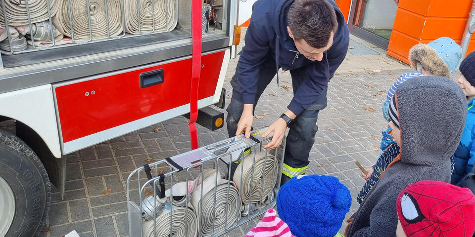 Ein Feuerwehrmann mit Schläuchen in einer Gruppe von Kindern.