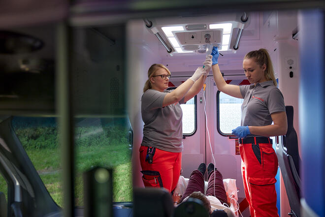 Sanitäterinnen versorgen liegende Person mit Infusion im Rettungsfahrzeug