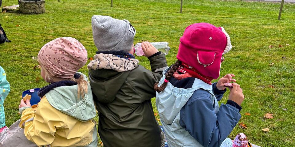Drei Kinder sitzen auf einer Holzbank und essen.