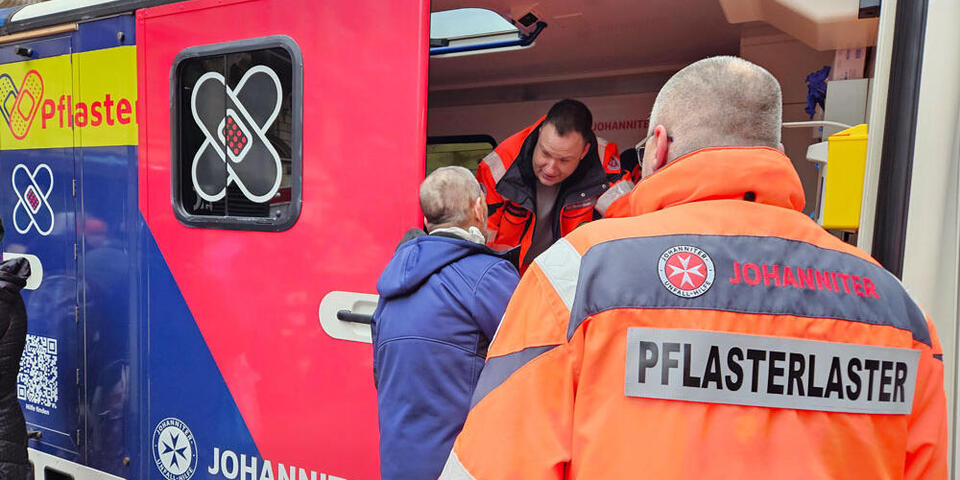 Drei Personen stehen an der Seite des Johanniter-Pflasterlaster. 