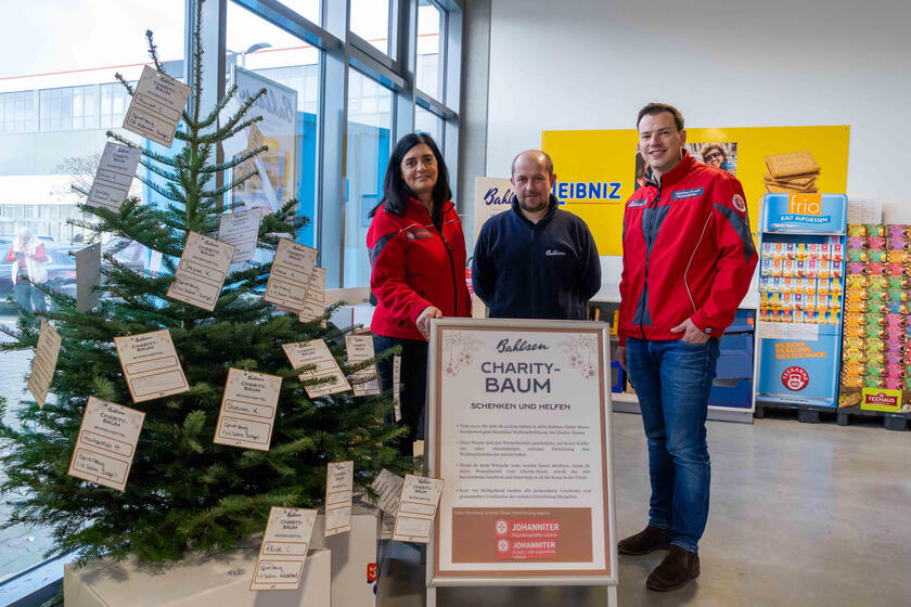 Lars Röhr (Mitte) von Bahlsen zeigt den mit Wünschen geschmückten Weihnachtsbaum im Bahlsen-Outlet Lübeck. Sandra David (l.) und Yonathan Arnold freuen sich über die Möglichkeit, Kindern ihrer Einrichtungen Wünsche zu erfüllen.