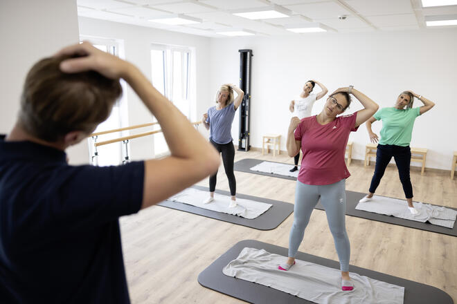 Eine Gruppe von Menschen macht eine Dehnungsübung, die ihnen von einem Trainer gezeigt wird.