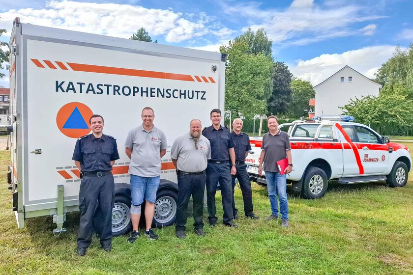 Sechs Personen stehen vor dem Kühlanhänger und einem Transportfahrzeug der Johanniter.