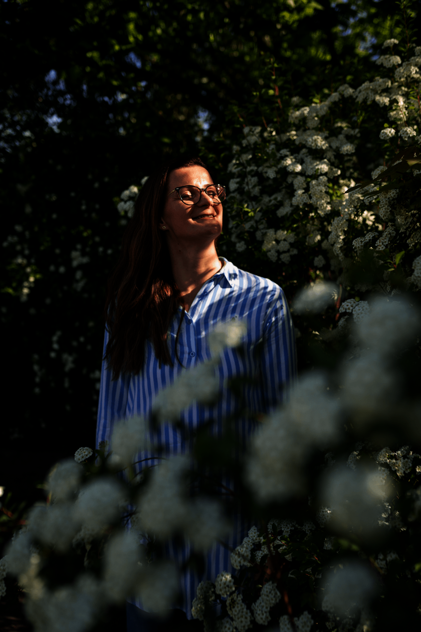 Frau steht zwischen blühenden Sträuchern und genießt die Sonne.  