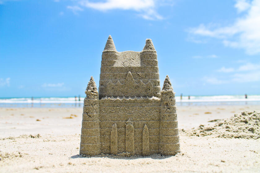 ein Schloss aus Sand an einem Strand, man sieht das Meer im Hintergrund