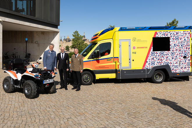 Auf dem Bild sind drei Personen zu sehen (Georg Khevenhüller, Christian Pegel, Volker Bescht) stehend neben zwei Einsatzfahrzeugen