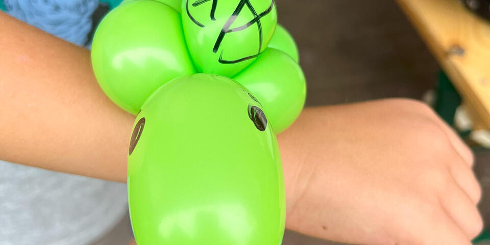 An einer Kinderhand ist ein grüner Luftballon in Form eines Tieres gebunden