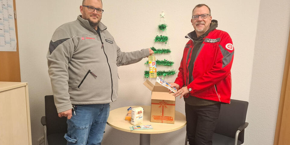 Zwei Männer mit einem offenen Paket. Einer steckt eine Flasche Öl hinein.