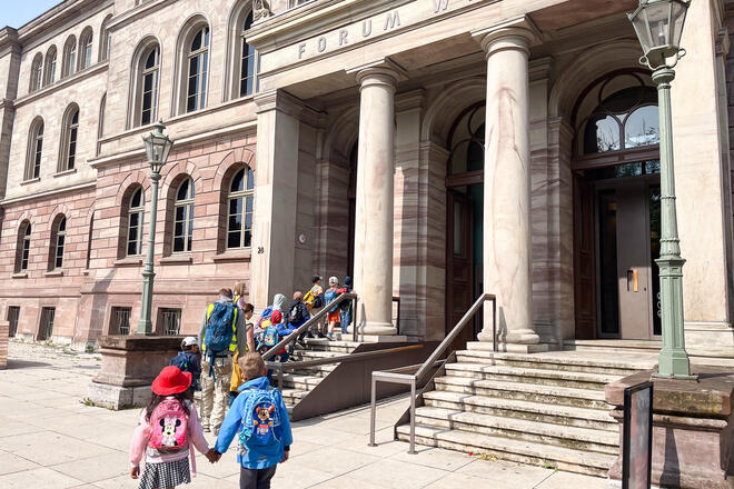 Kinder und Erwachsene vor einem großen Gebäude mit Säulen.