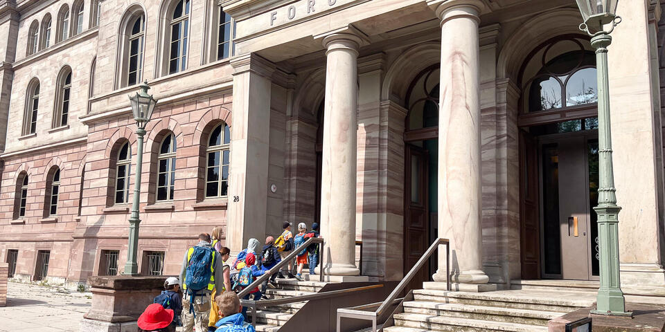Kinder und Erwachsene vor einem großen Gebäude mit Säulen.