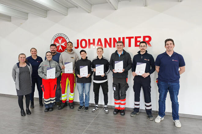 Sechs junge Menschen in Rettungsdienstbekleidung mit einer Urkunde in der Hand. rechts und links daneben weitere Personen
