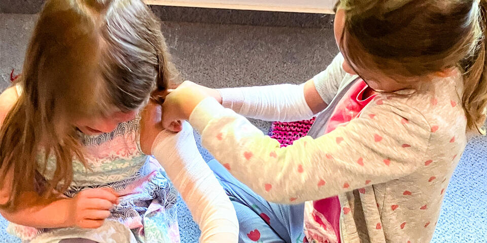 Ein Mädchen legt einem anderen Mädchen einen Verband am Arm an
