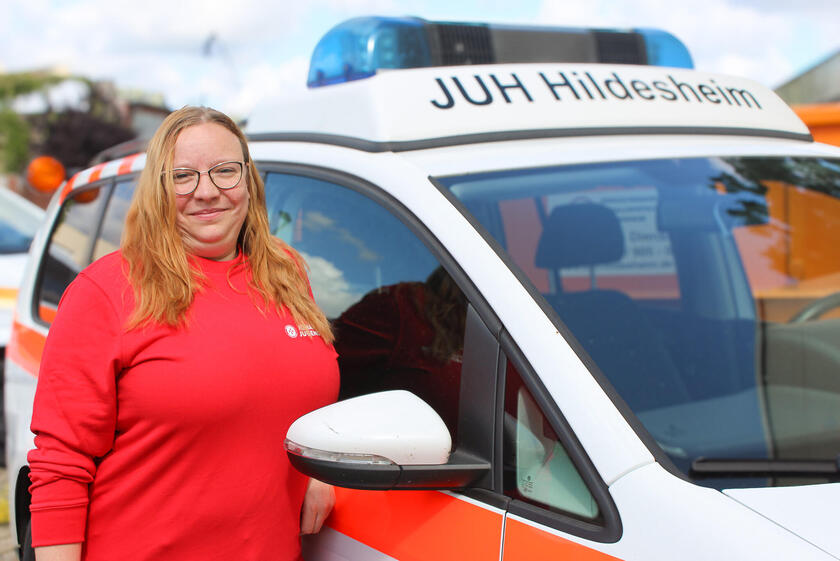 Ein Frau mit einem roten Johanniter-Jugend-Pulli an einem Johanniter-Fahrzeug