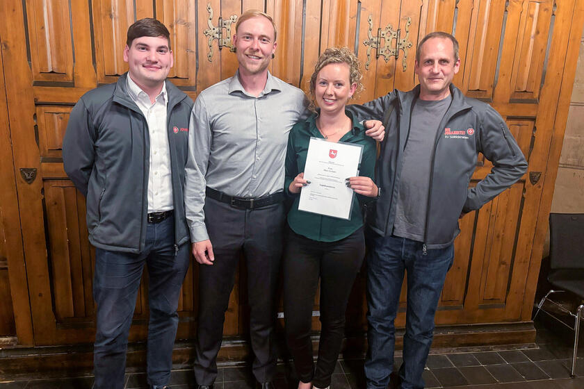 Eine junge Frau mit einer Urkunde steht neben drei Männern, zwei davon haben eine Johanniter-Jacke in der Hand