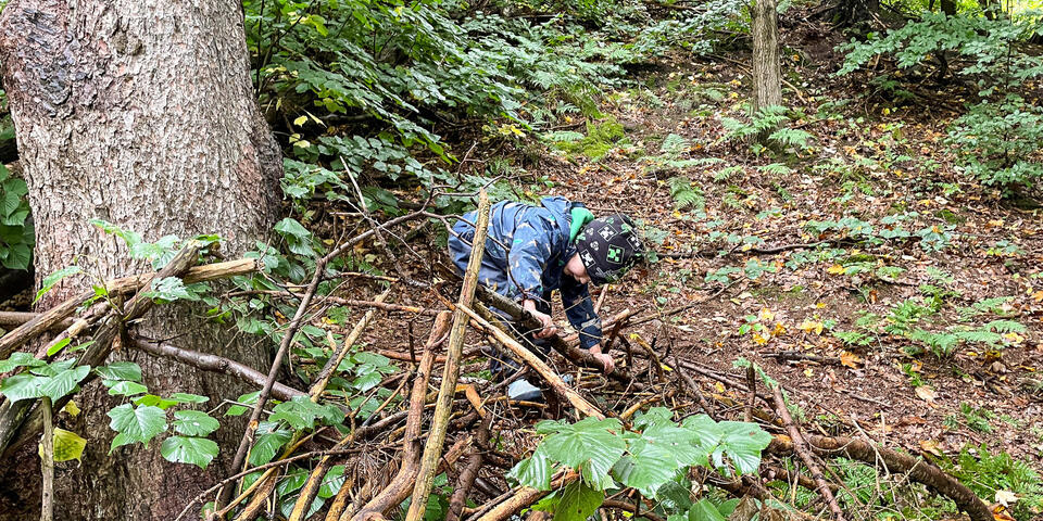 Ein Kind baut aus Ästen in einem Wald ein Zelt.