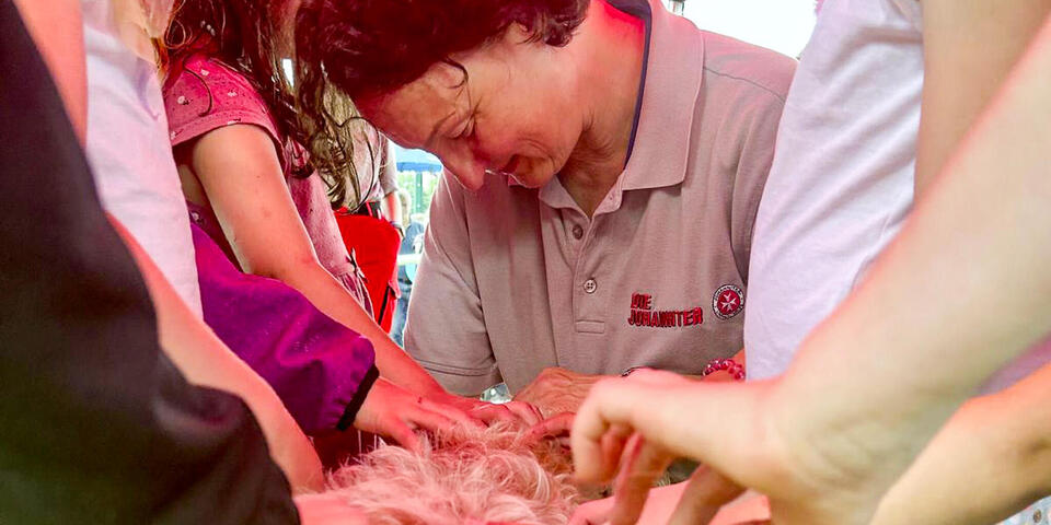 Eine Johanniterin mit einem Hund, der von Kinderhänden gestreichelt wird
