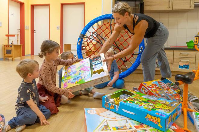 Neue Spielsachen für die Kleinen Hanseaten Die Kitaleiterin überreicht das eine Kiste mit Spielzeug an zwei Kinder.