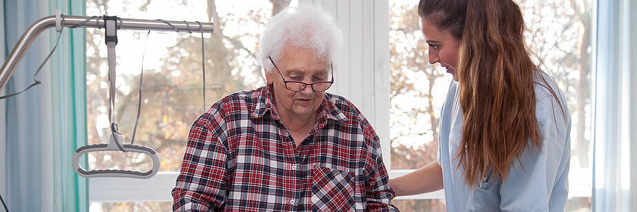 Älterer Patientin an Rollator wird von Schwester geholfen 