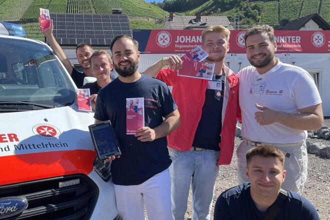 Johanniter halten freundlich einen Flyer zum Thema Fördermitgliedschaft in die Kamera