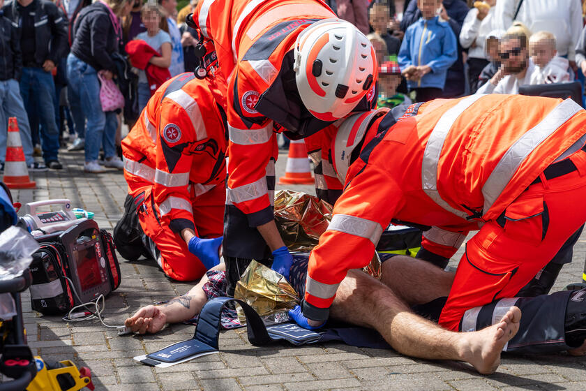 Drei Rettungskräfte der Johanniter versorgen einen am Boden liegenden Mann, der von einem Gerüst gestürzt ist.