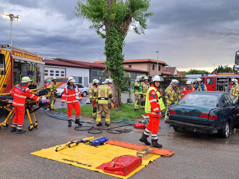 Viele Personen von dem Johanniter-Bevölkerungsschutz Heilbronn und der Feuerwehr, üben zusammen die Situation nach einem Verkehrsunfall. Geübt wird an einem PKW. Eine Plane liegt ausgebreitet auf dem Boden, darauf liegen verschiedene Werkzeuge. Ein Sanitäter schiebt eine Trage.