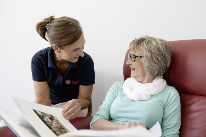 Eine Mitarbeiterin in der Tagespflege der Johanniter schaut gemeinsam mit einer Seniorin in ein Fotoalbum.