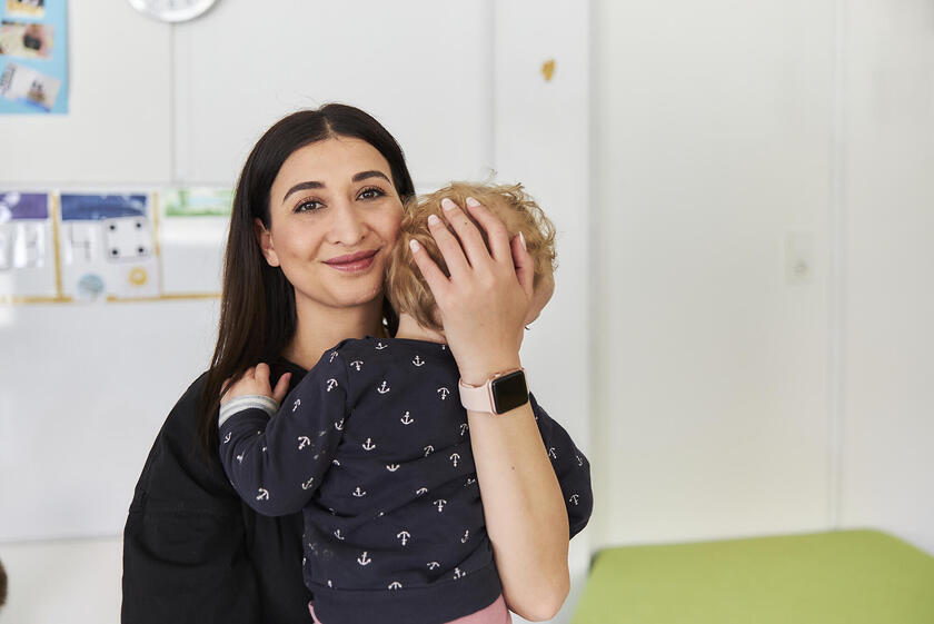 Eine lächelnde junge Frau hält beschützend ein Kind in ihren Armen