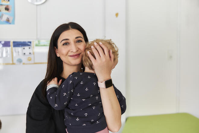 Eine lächelnde junge Frau hält beschützend ein Kind in ihren Armen