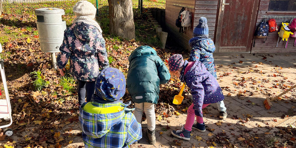 Kinder schieben einen Laubhaufen zusammen