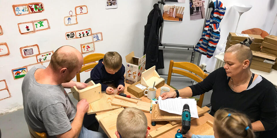 Eine Frau, ein Mann und drei Kinder sitzen um einen Tisch und basteln