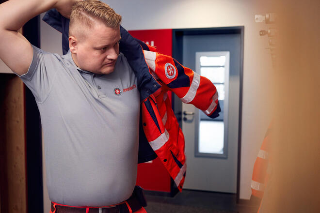 Ein Ehrenamtliche der Johanniter zieht sich eine Einsatzjacke an.