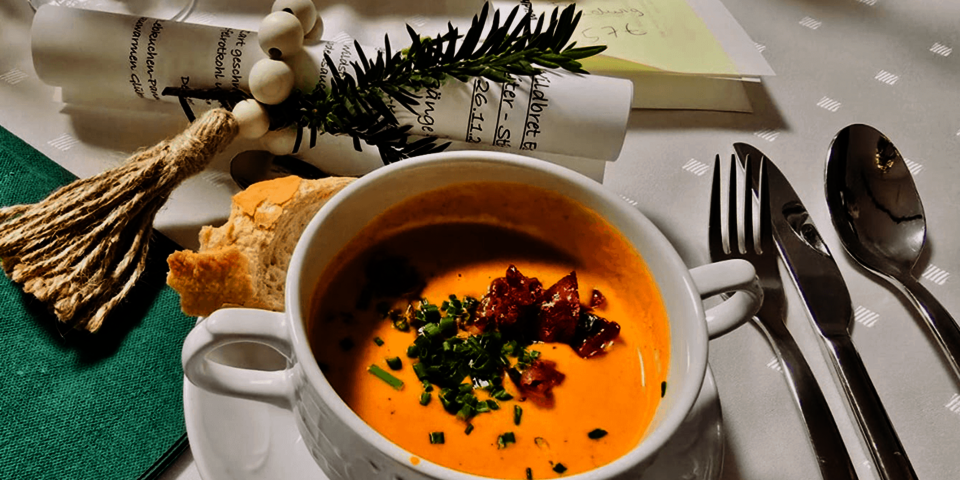Teller mit cremiger Suppe, garniert mit Kräutern und Speck, dazu ein Stück Brot, Besteck und weihnachtliche Tischdeko