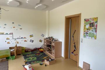Innenbereich der Kita Pustewind mit einem Spielteppich, Spielzeug, einer beschmückten Wand und Tür