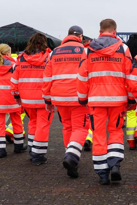 Zu sehen sind sieben ehrenamtliche Helferinnen und Helfer in Dienstkleidung von hinten
