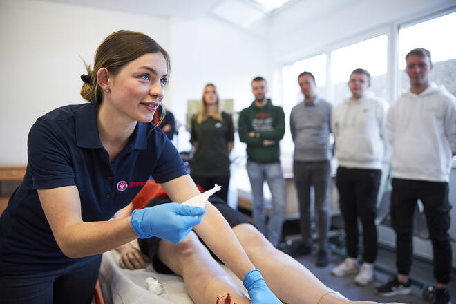 Eine Ausbilderin der Johanniter zeigt den Teilnehmenden in einem Erste-Hilfe-Kurs, wie man eine Wunde versorgt.