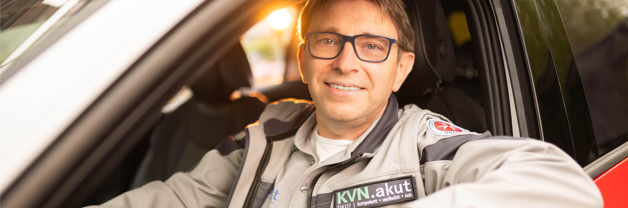 Ein Fahrer im ärztlichen Bereitschaftsdienst sitzt in einem Fahrzeug und schaut in die Kamera.