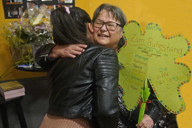 Eine Frau wird von einer anderen Frau umarmt und hält ein Papierkleeblatt mit Innschrift