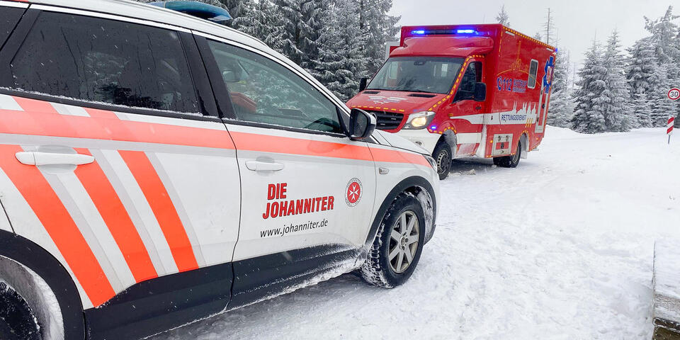Ein RTW und ein Johanniter-Fahrzeug im Schnee. Im Hintergrund schneebedeckte Bäume.