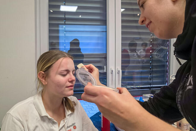 Eine Helferin der Johanniter schminkt einer Verletztendarstellerin das Gesicht.